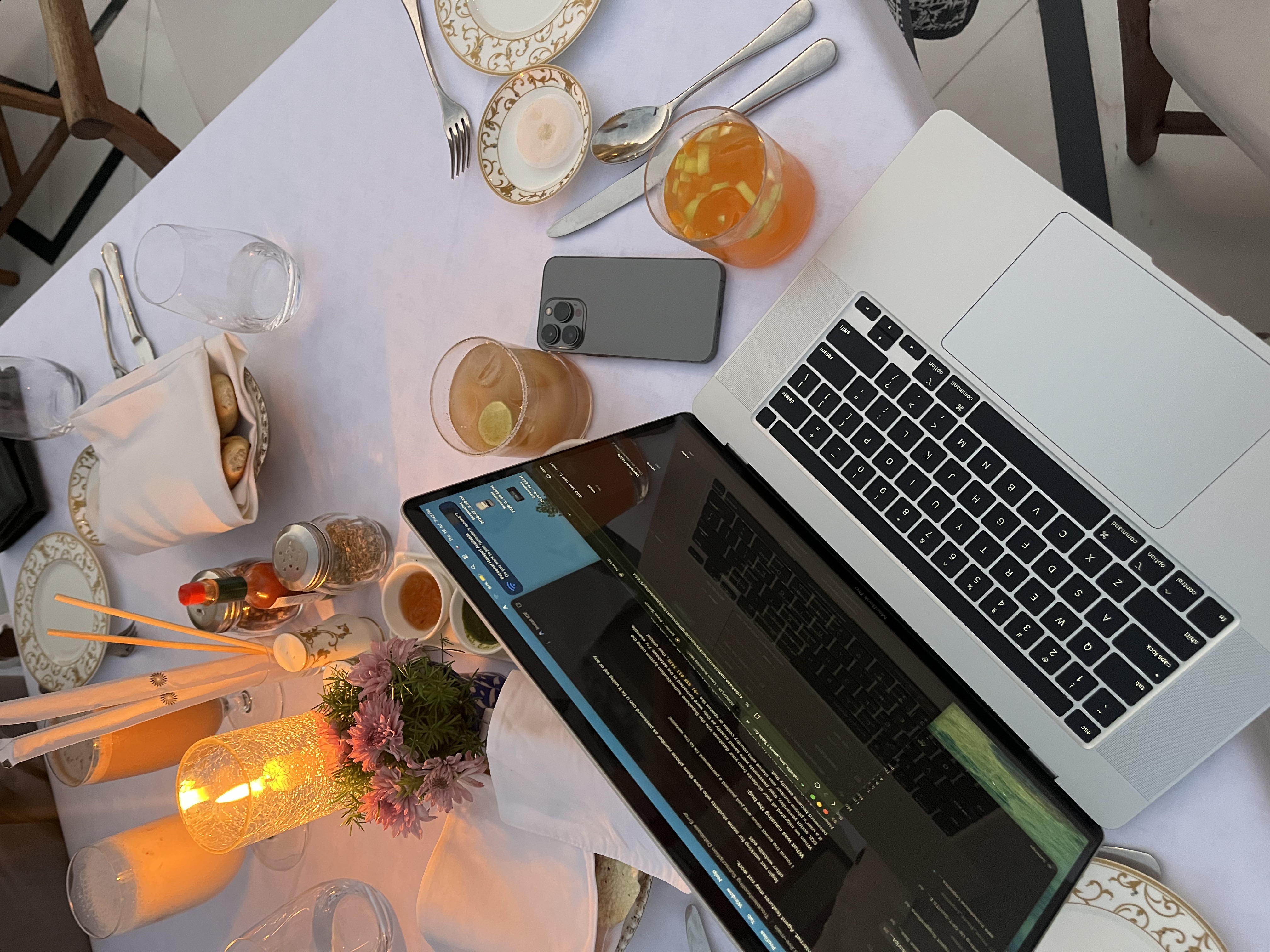 A laptop open with code at a candlelit dinner table